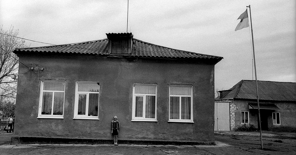 Black and white picture of a soviet style orphanage exterior with a child standing out front