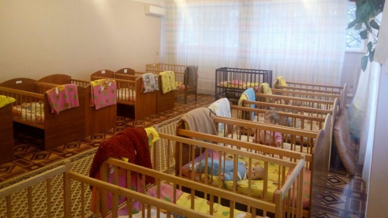 Cribs lined up along the walls of a small room in a baby institution in Ukraine