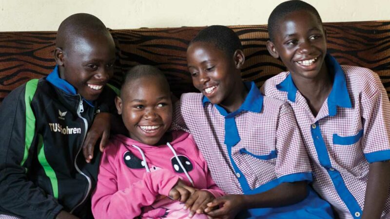 Four Rwandan siblings sit on the sofa close together, laughing