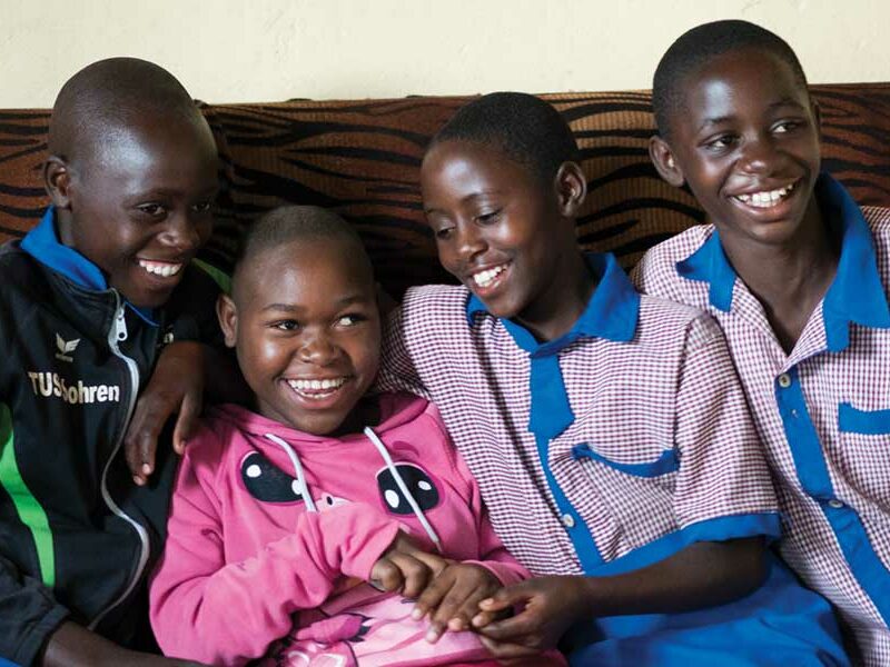 Four Rwandan siblings sit on the sofa close together, laughing