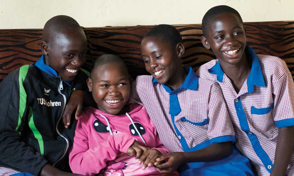 Four Rwandan siblings sit on the sofa close together, laughing