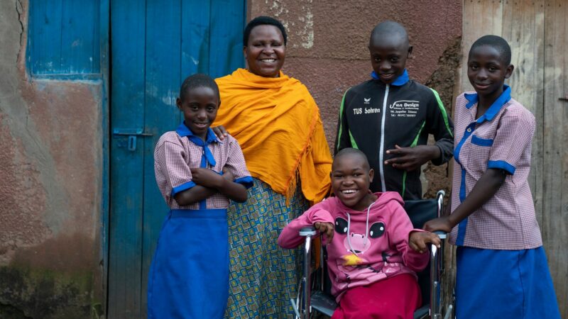A Rwandan teenage girl in her wheelchair surrounded by happy family members outside their front door