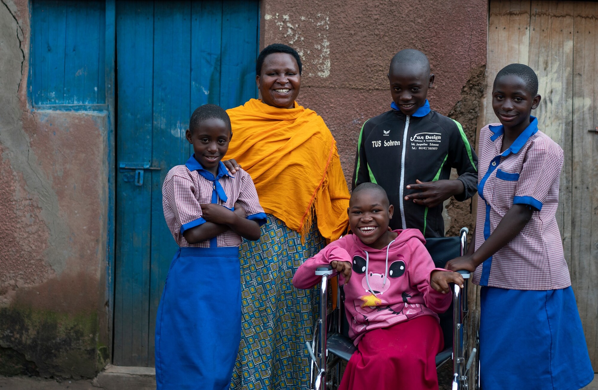 A Rwandan teenage girl in her wheelchair surrounded by happy family members outside their front door