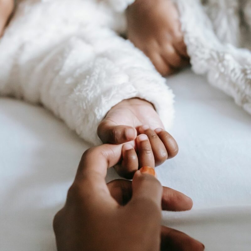 A newborn baby clutches at a parent's hand