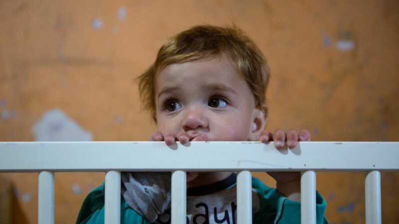 A child at risk of ending up in an orphanage, peeking their face over the edge of a cot
