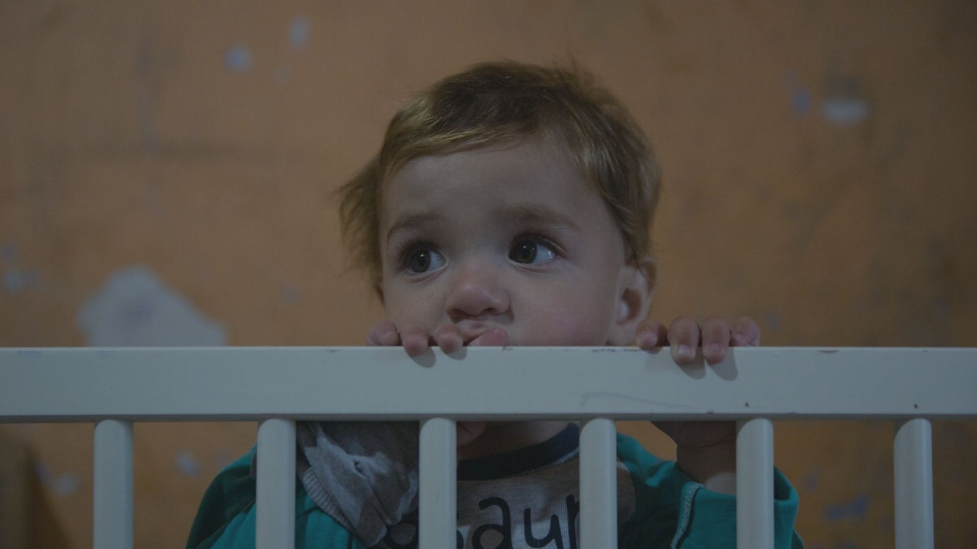 Child at risk of ending up in an orphanage peeking over the edge of their cot