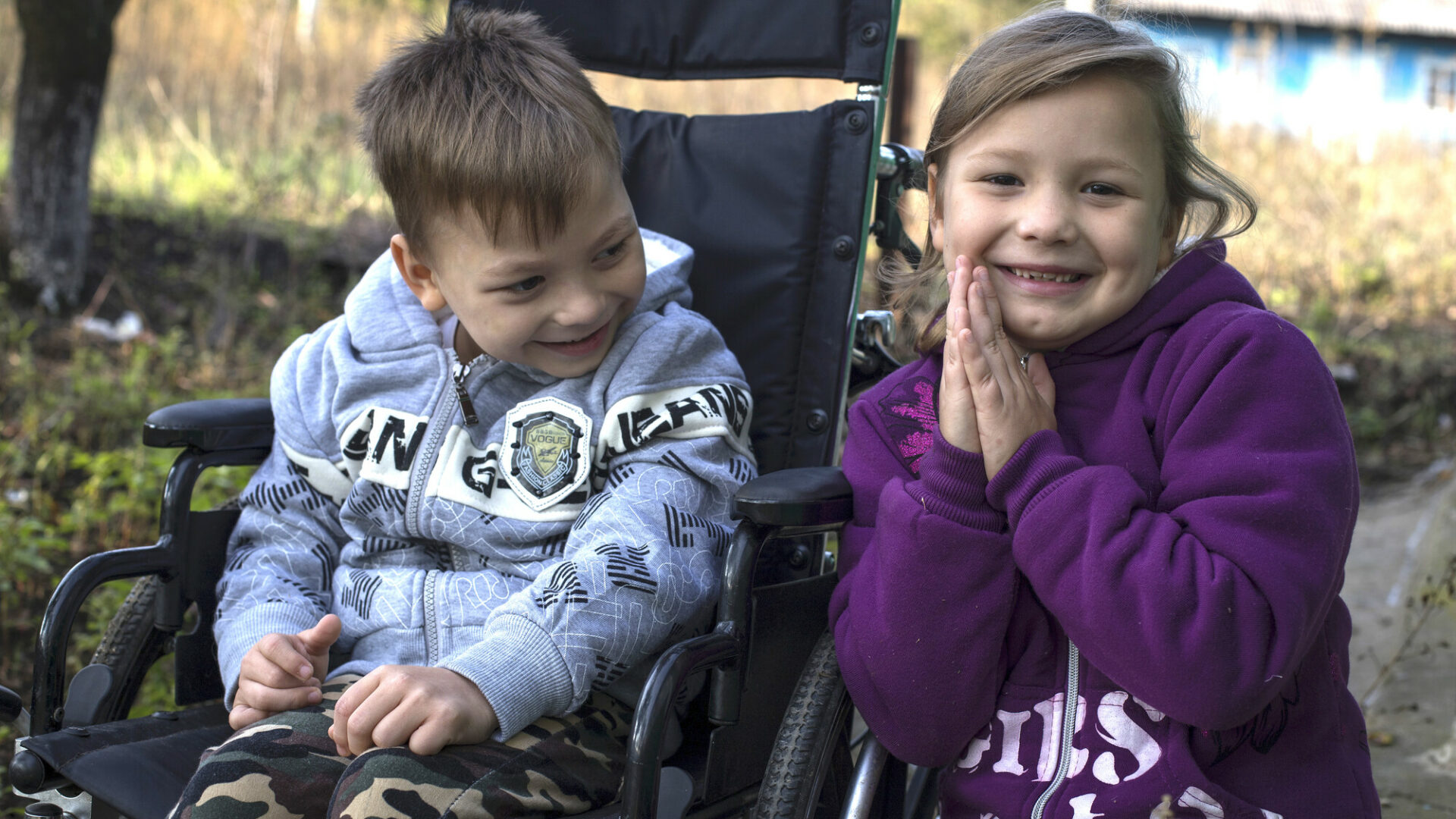 A Moldovan boy in a wheelchair and his little sister next to him smile at the camera