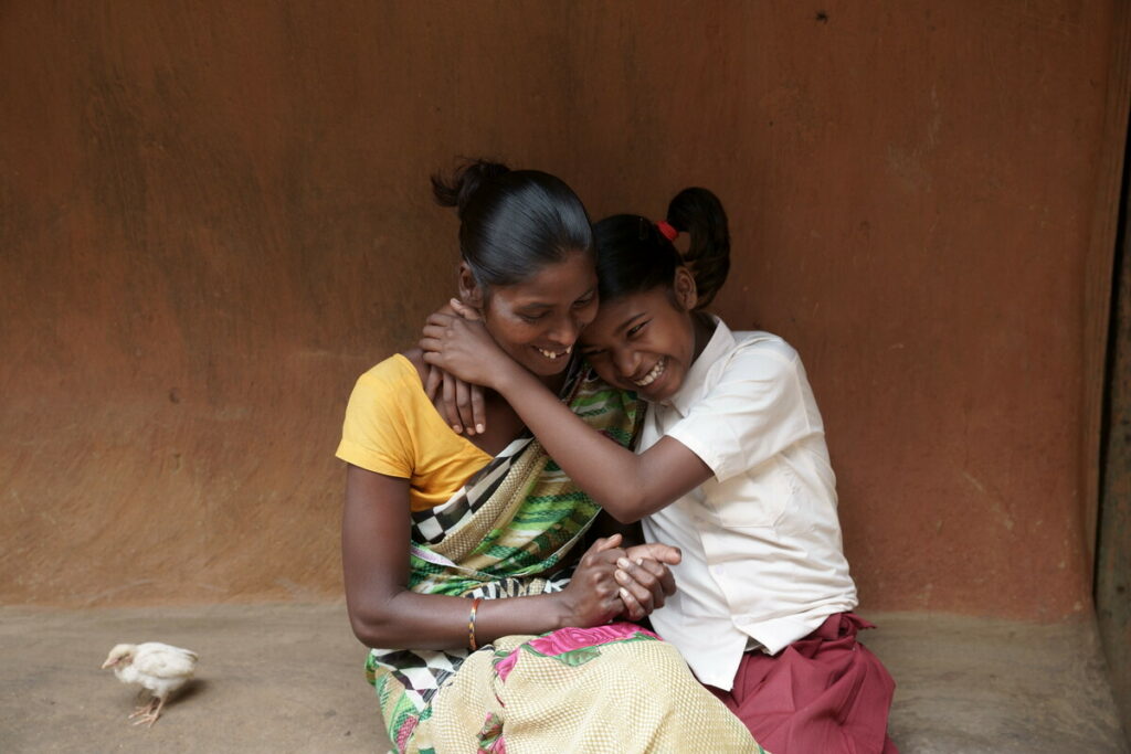 Photo of a young girl called Sonia hugging her mother outside their house in rural India