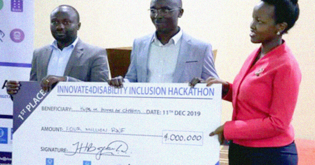 Two Rwandan men and a woman in a red suit jacket stand holding a giant cheque and smiling