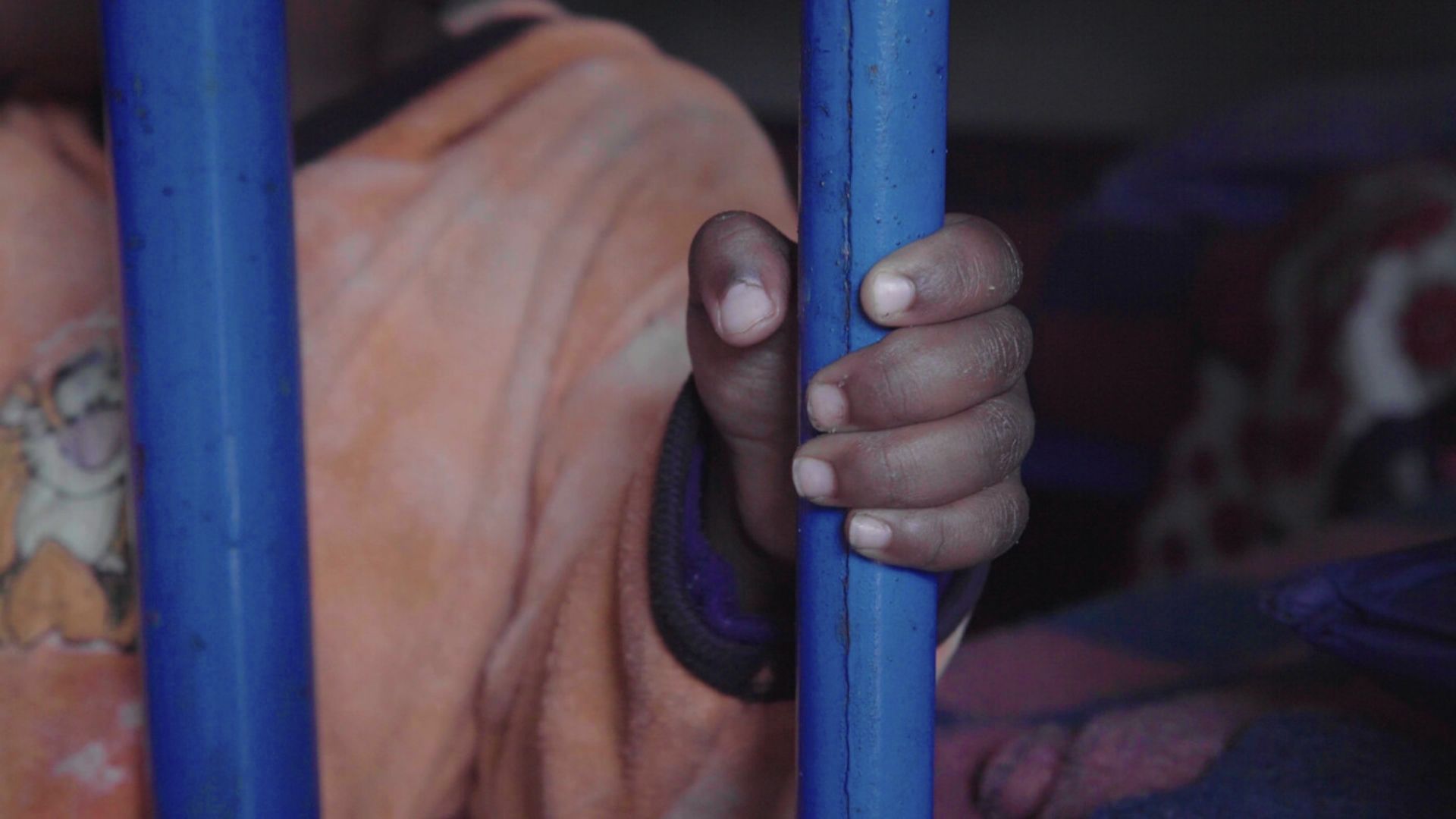 A child's hands on metal bars in an institution in Kenya