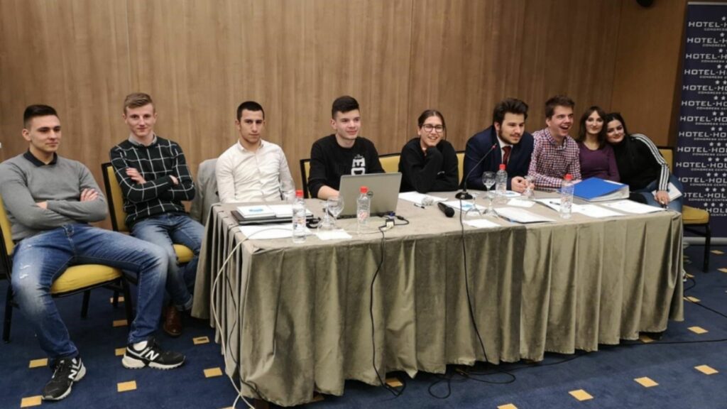 A table in a conference room with young people sitting along it smiling
