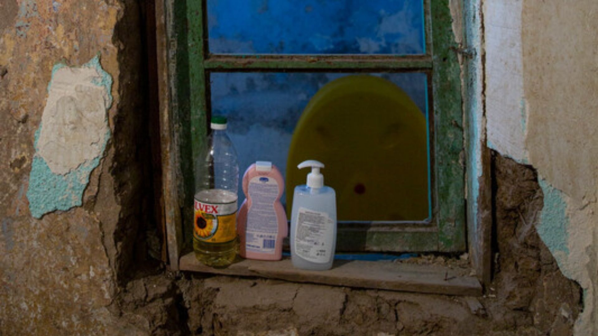 Olive oil and soap balance on the window ledge of a house in Romania. The window shows the signs of poverty.