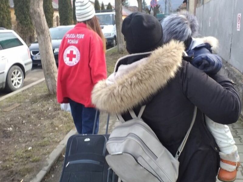A woman carrying a child alongside a red cross staff member, during the Ukraine humanitarian crisis in 2022