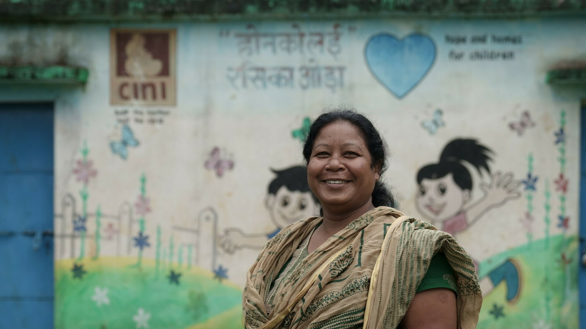 Indian woman standing smiling in front of colourful wall mural