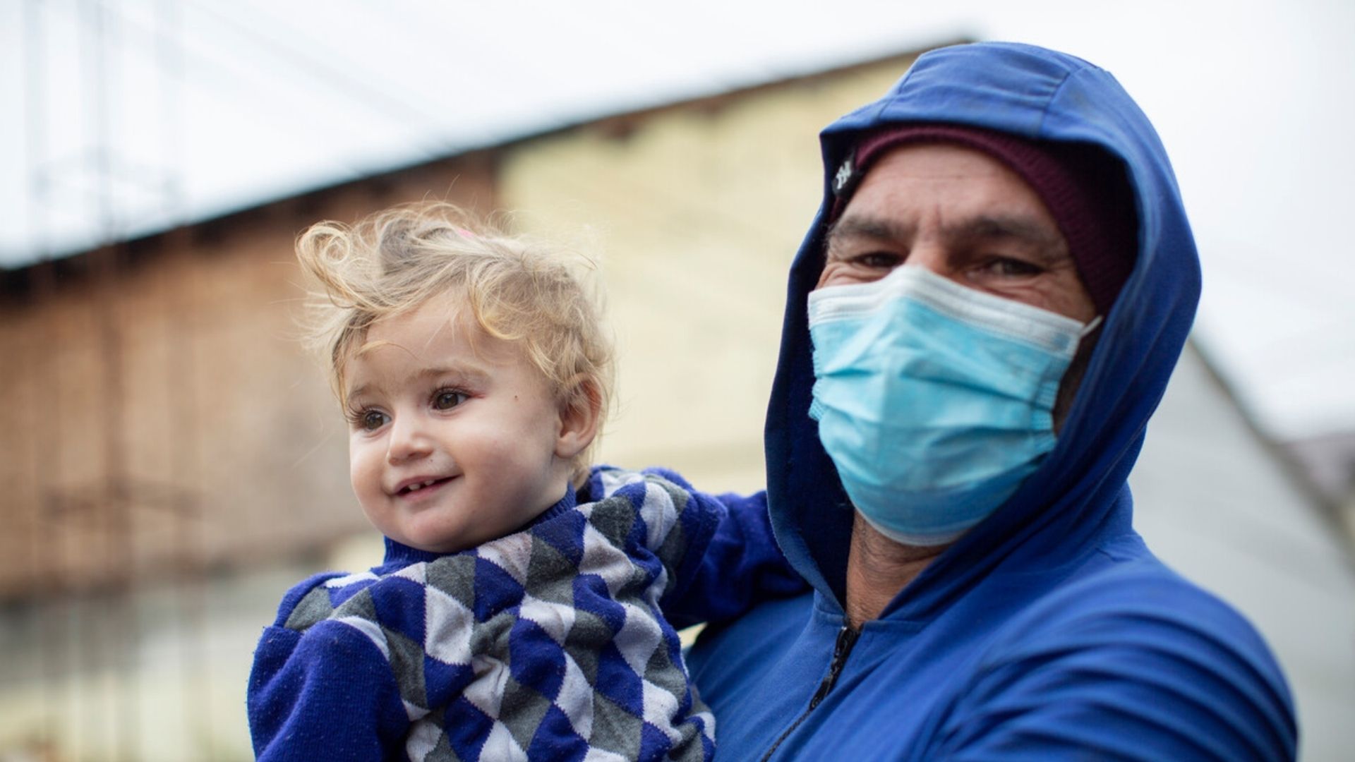The father holds his youngest daughter outside with mask on