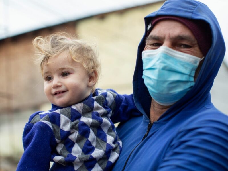 A father holds his youngest daughter outside with mask on. We supported this family as part of our programmes in Romania