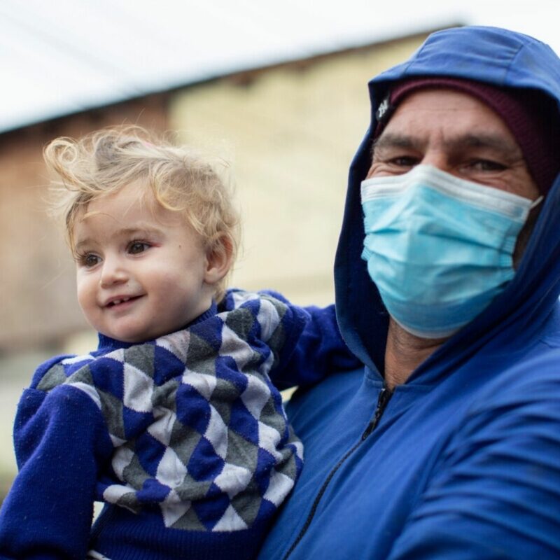 A father holds his youngest daughter outside with mask on. We supported this family as part of our programmes in Romania