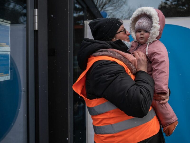 Scenes from the border between Romania and Ukraine during the crisis. A child is being held by a man in a high visibility vest while it snows.