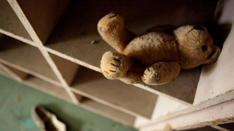 An abandoned teddy bear sits in a wooden cubby hole in a dingy room