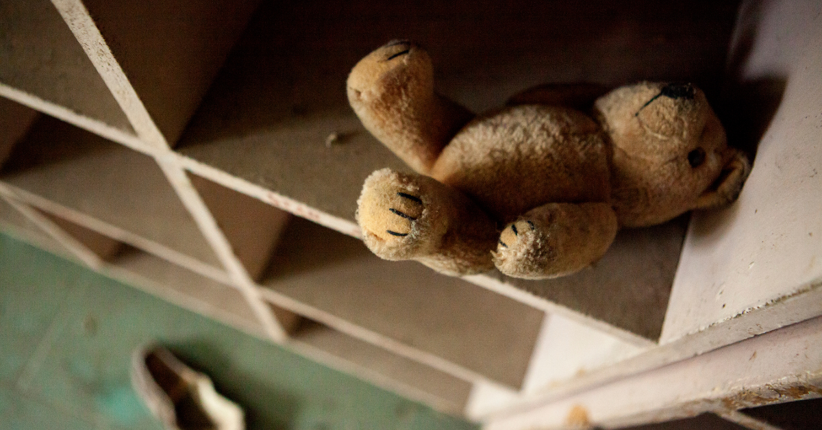 An abandoned teddy bear sits in a wooden cubby hole in a dingy room