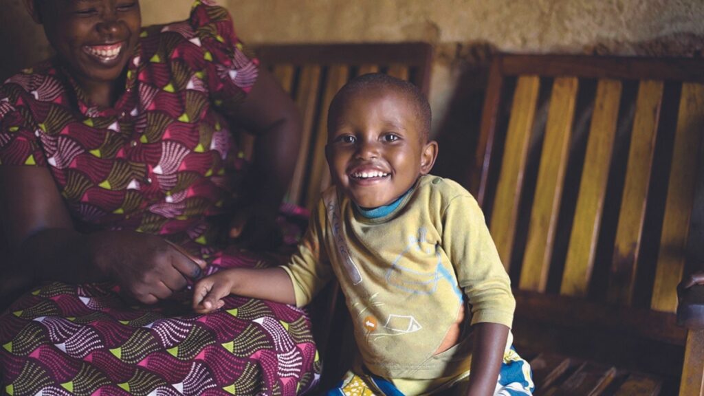 A young Rwandan girl, Therese, smiles as she leans on her mother Valerie's lap