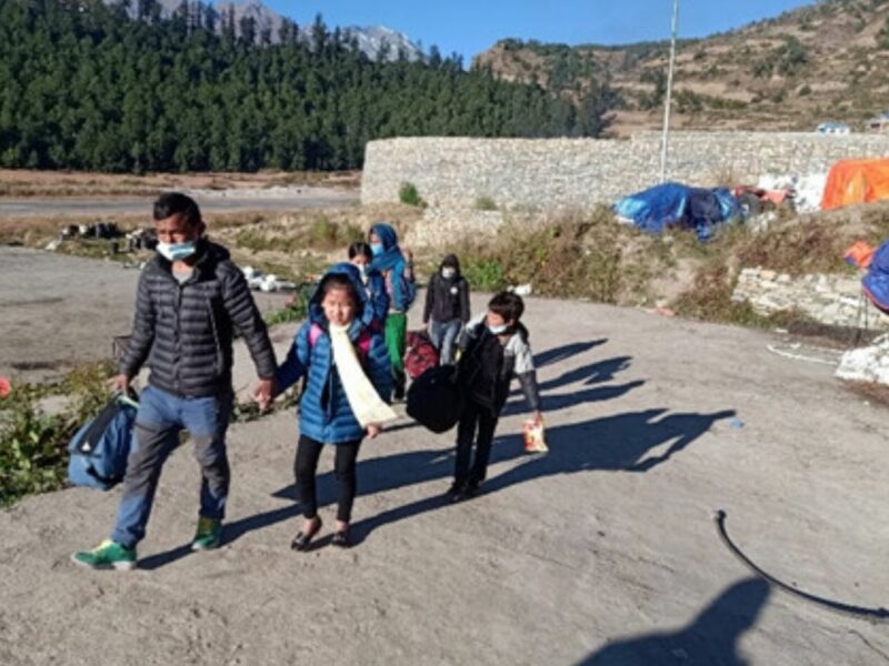 Nepali man leads 4 warmly dressed children across some tarmac outside a landing strip