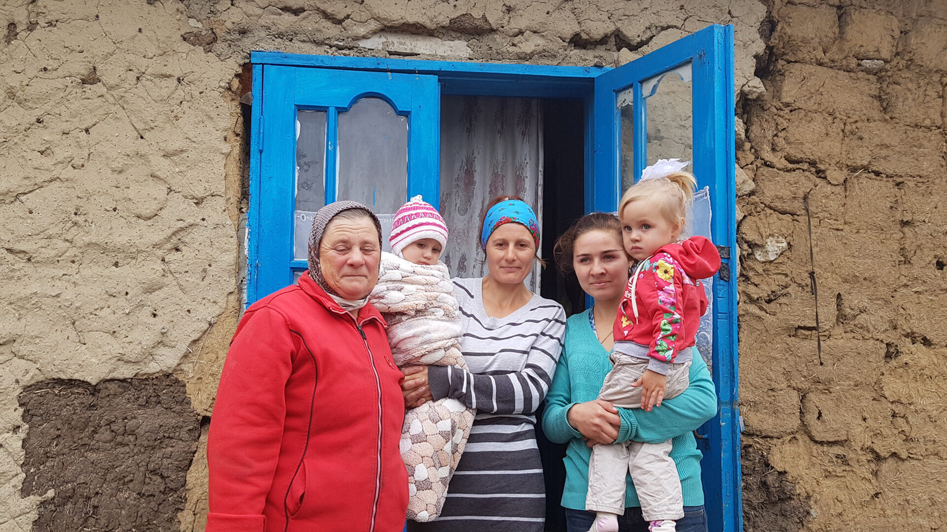 A group of warmly dressed female family members stand outside the bright blue door to their home
