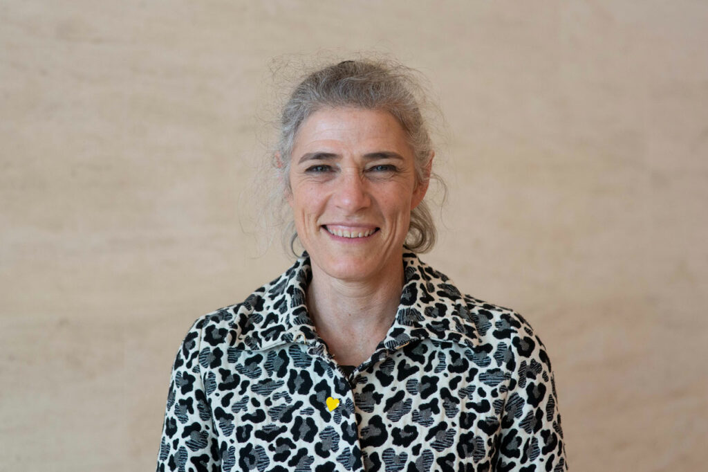 Anna Segall wears a patterned shirt and smiles at the camera in front of a plain background