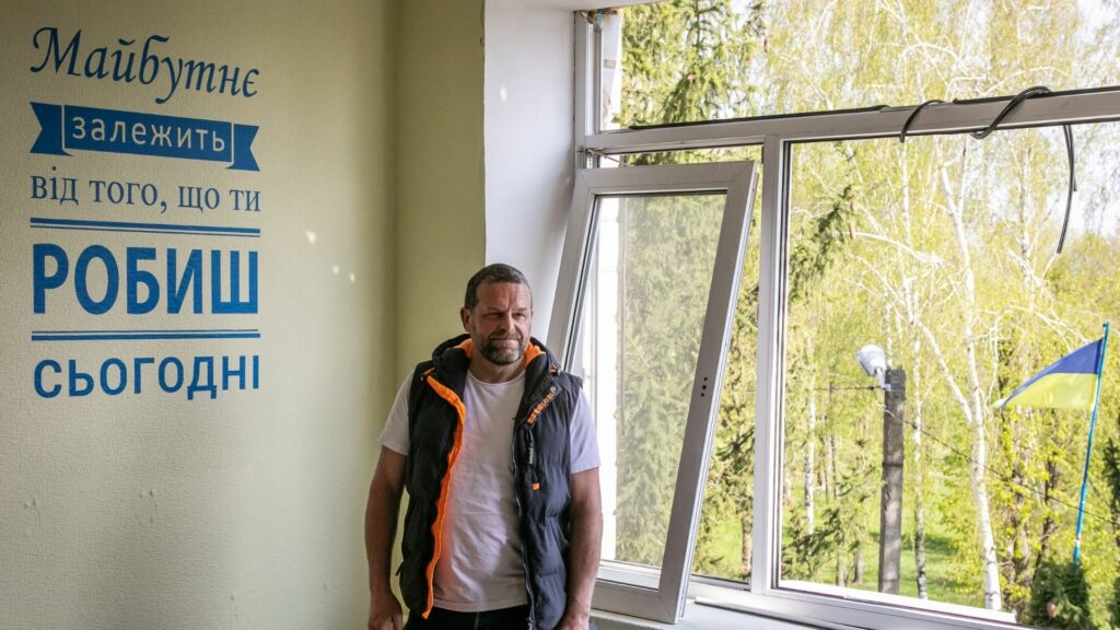 Mark Waddington standing in front of a quote by Ghandi in a bombed Ukrainian school