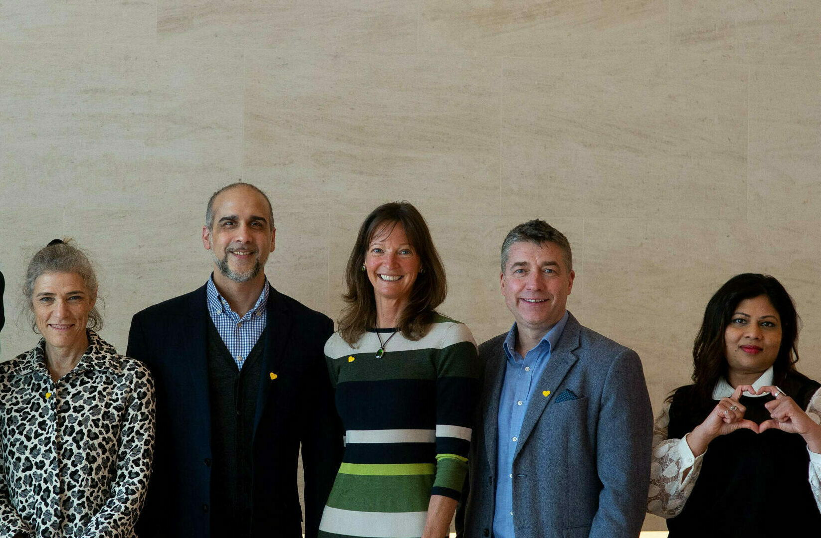 3 men and 3 women stand against a plain background, smiling for the camera