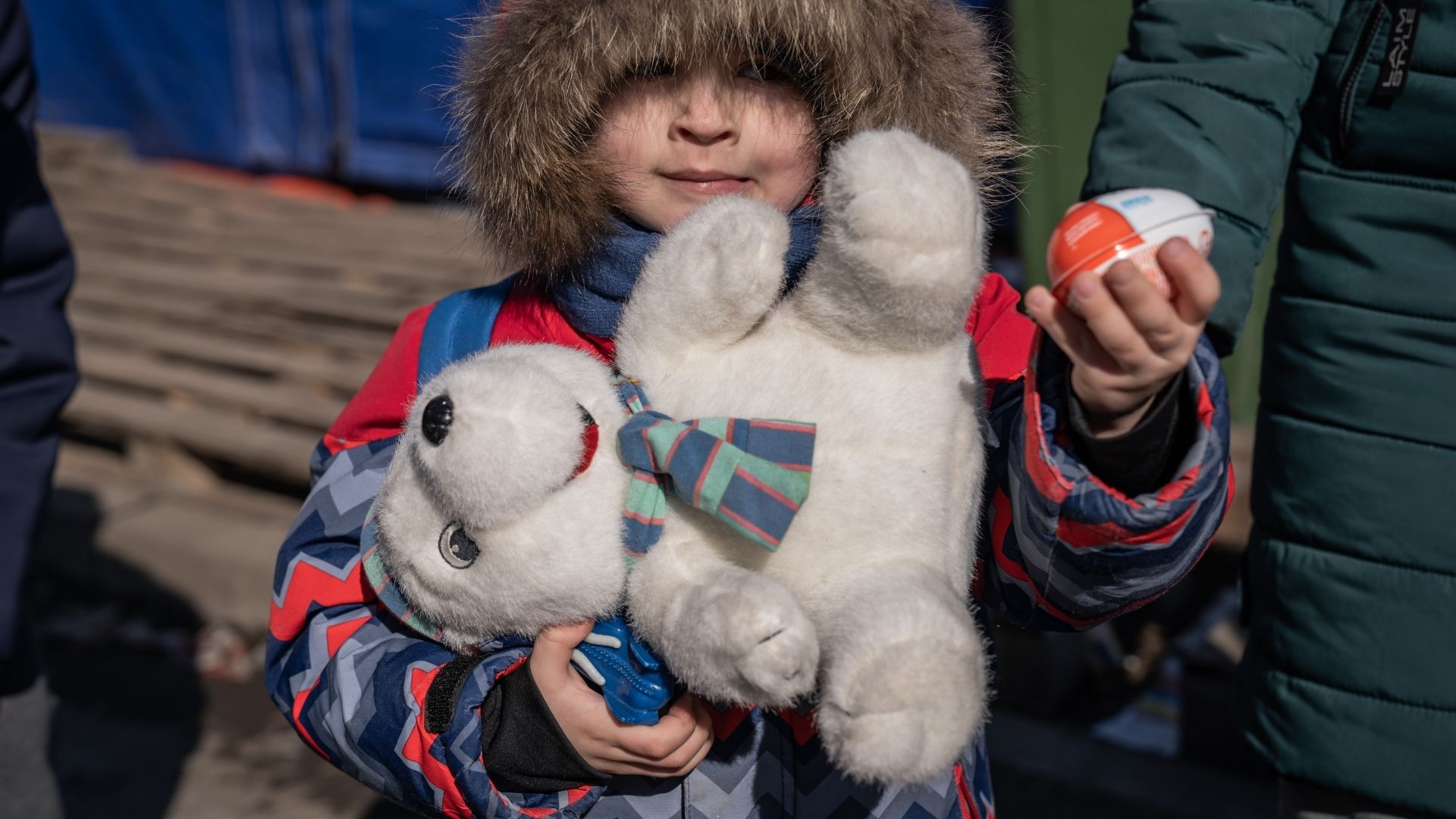 A child carrying a teddy bear, holding their parent's hand,