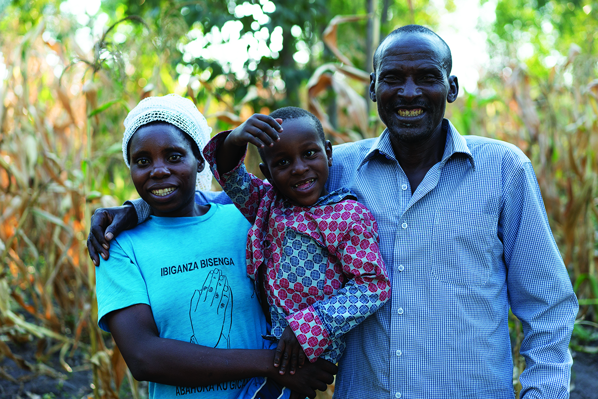 A Rwandan boy, Carrol, is held by his mother, as his father wraps his arm around her shoulder.