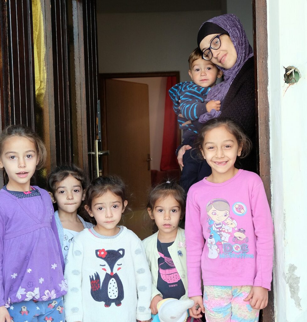 Esmerelda holds her young son in the doorway of her flat, as five girls stand in the foreground looking at the camera