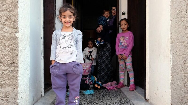 Esemerelda stands in the doorway of her flat with four of her children, smiling at the camera