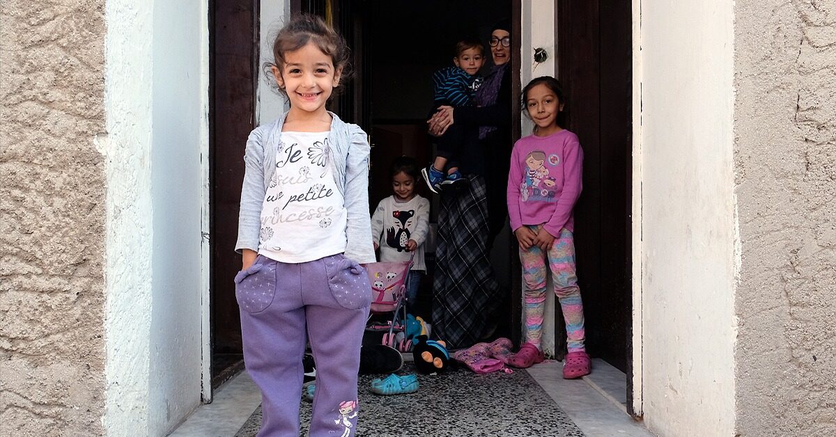 Esemerelda stands in the doorway of her flat with four of her children, smiling at the camera