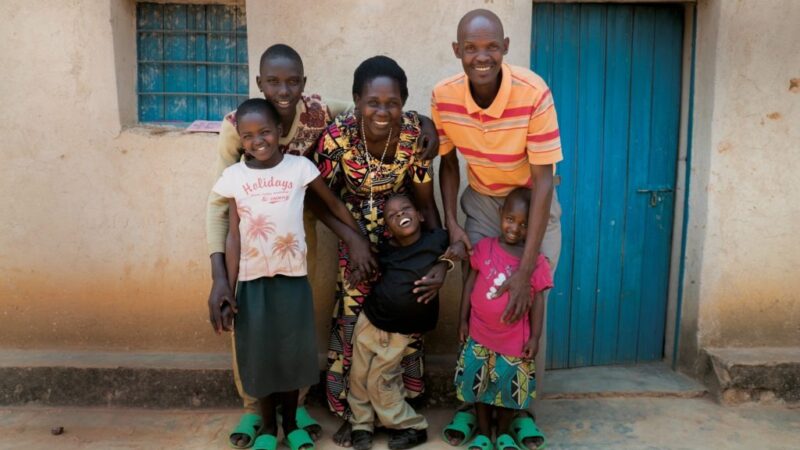 A family stands outside a house in Rwanda, smiling at the camera