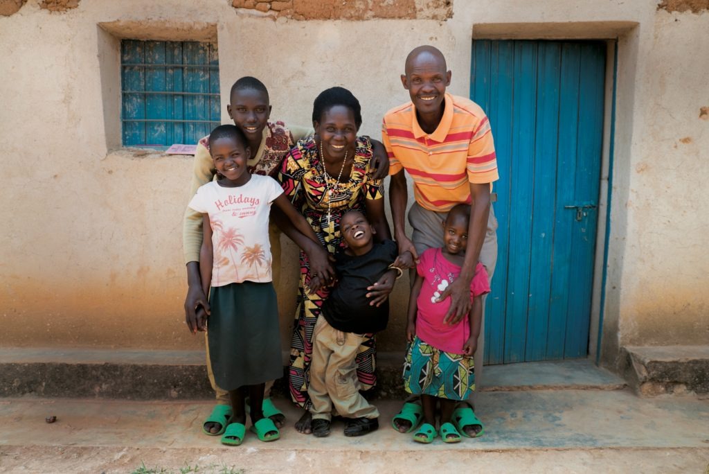 A family stands outside a house in Rwanda, smiling at the camera