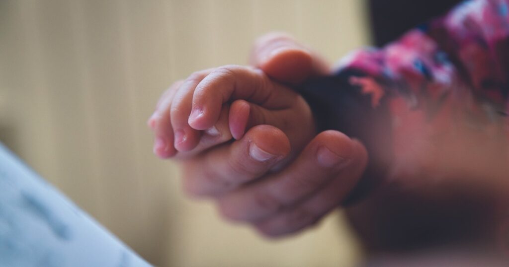 A mother holding her young child's hand.