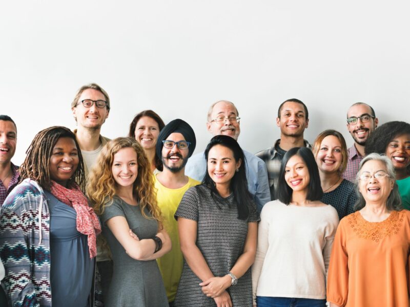 A diverse group of people standing together against a blank wall, smiling