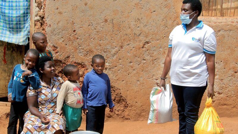 A Rwandan mother, Valerie, crouches, surrounded by her four children outside their home