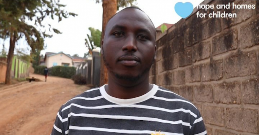 A portrait of Eric standing by a wall in a quiet street in Rwanda.