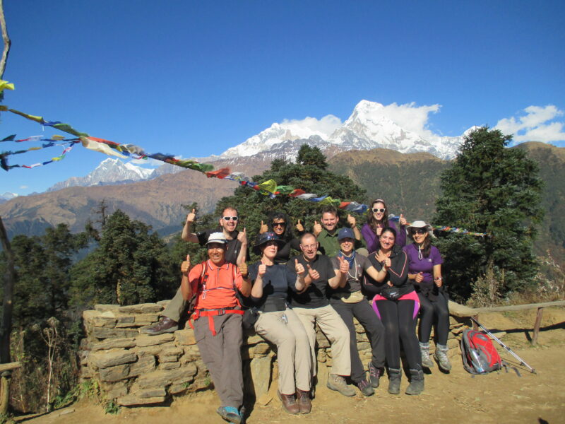 Group of trekkers sit on a stone wall in front of Himalayan mountainscape