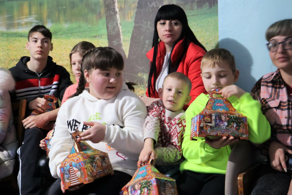 Image is of children and adults sat together receiving gifts