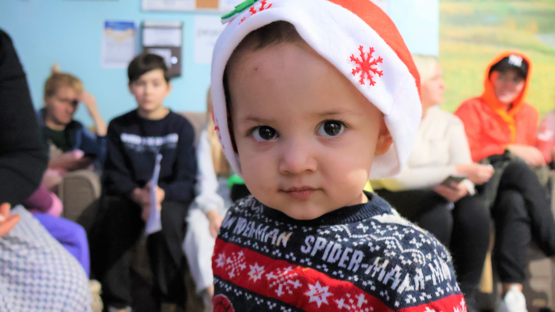 Image is of a young children in a Santa hat and Christmas jumper