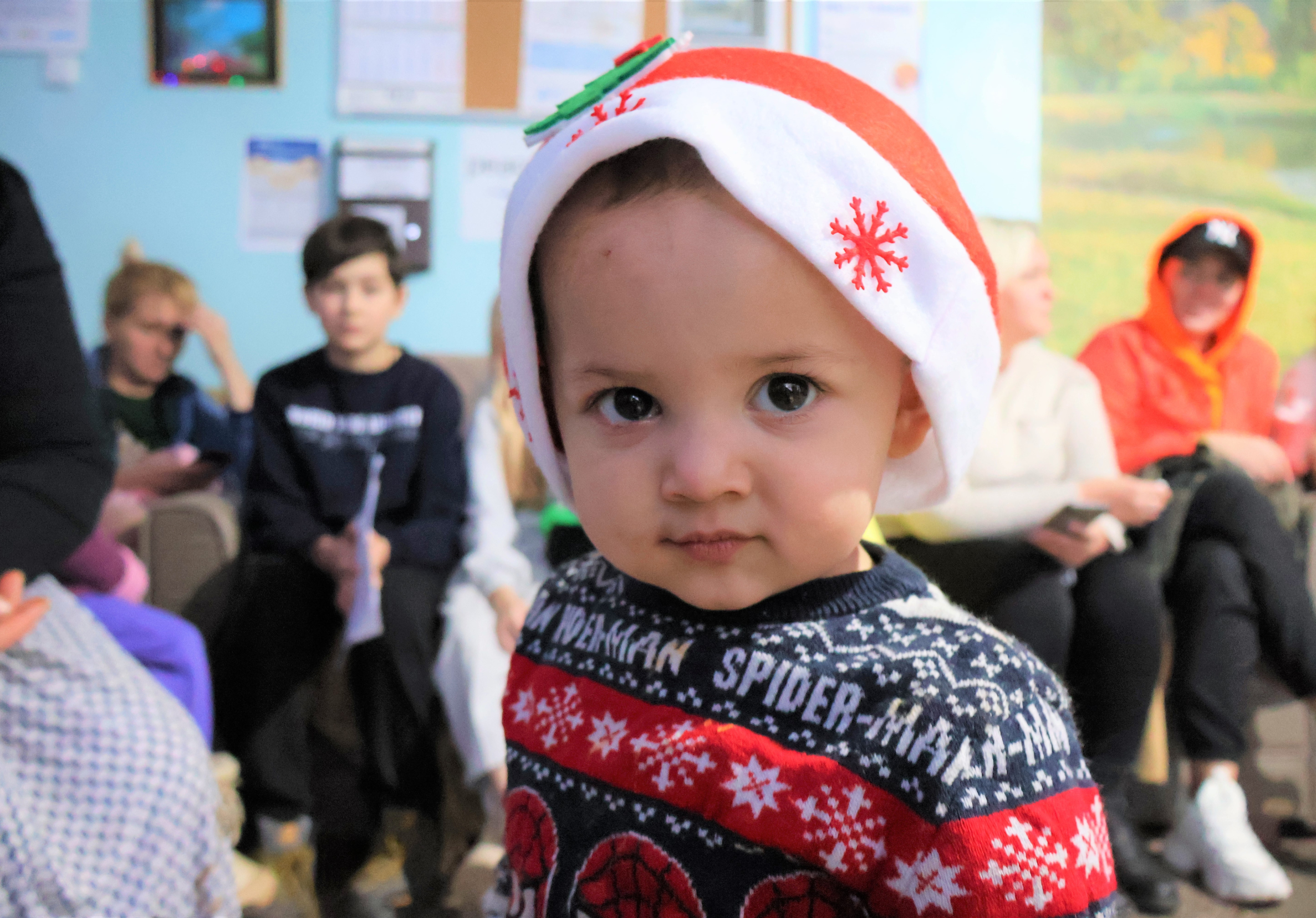 Image is of a young children in a Santa hat and Christmas jumper