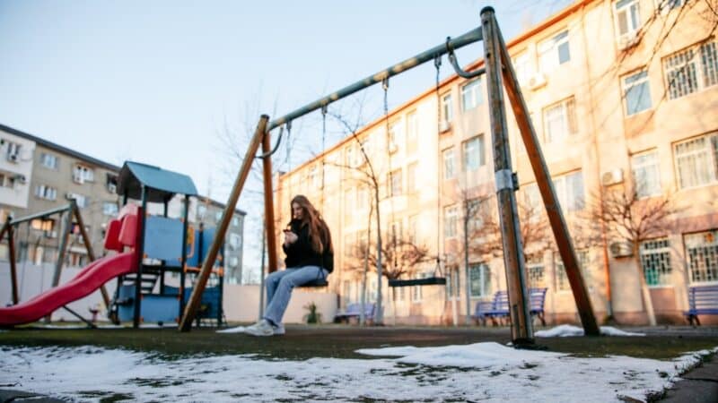 A photo of Daryna*, a young orphanage evacuee from Ukraine, sitting on a swing looking sad and alone.