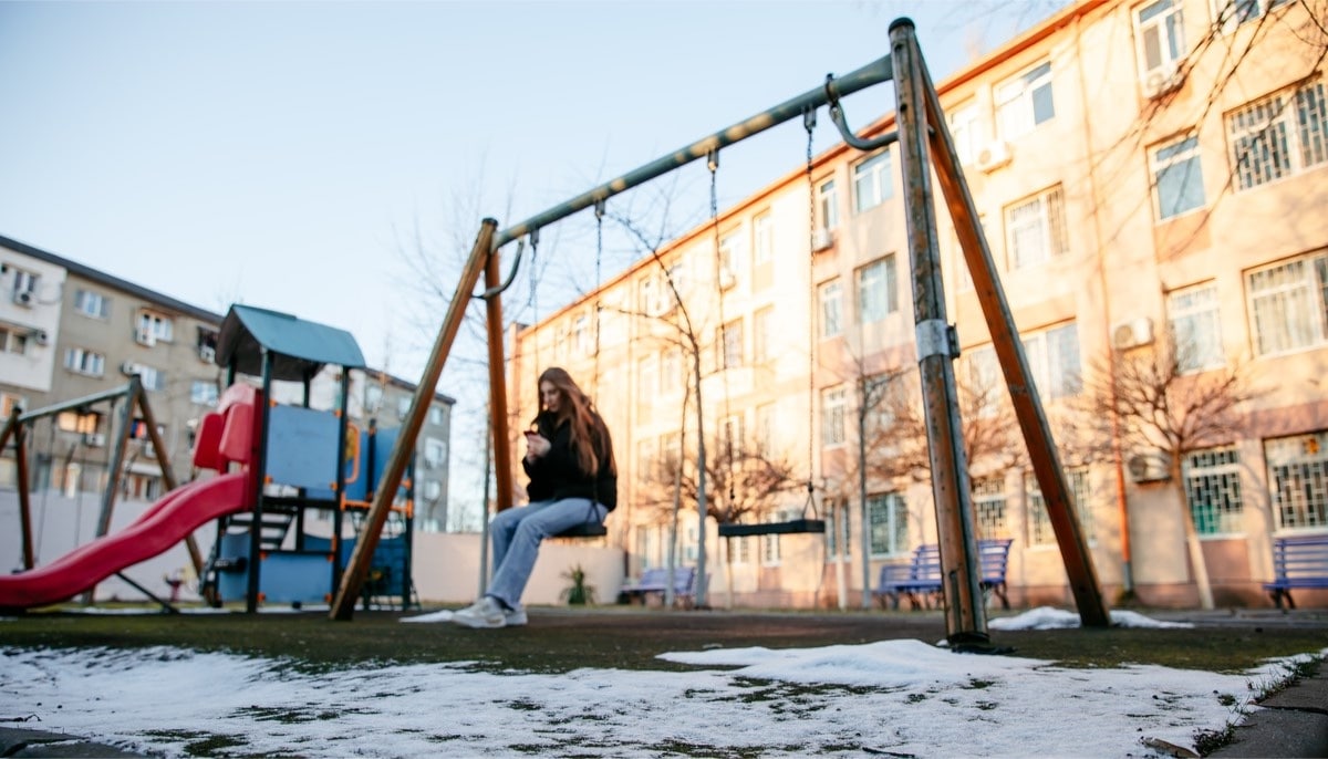 A photo of Daryna*, a young orphanage evacuee from Ukraine, sitting on a swing looking sad and alone.