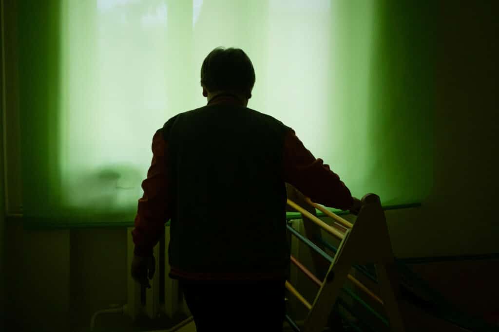 Andrii* a Ukrainian boy with autism stands in a darkened room with green curtains