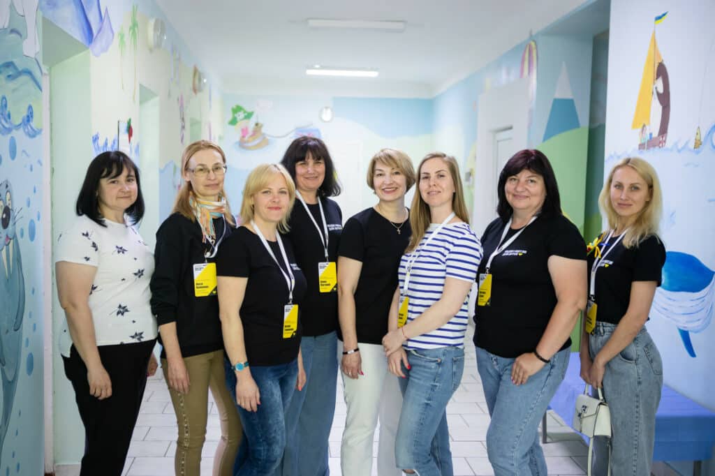7 female Ukrainian staff stand proudly inside the Fastiv Children's Spot - a bright community centre with pictures on the walls