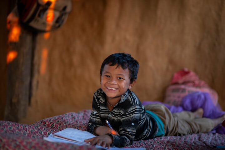 Sunil lying on his bed doing schoolwork, with supplies provided by Hope and Homes for Children's partners.